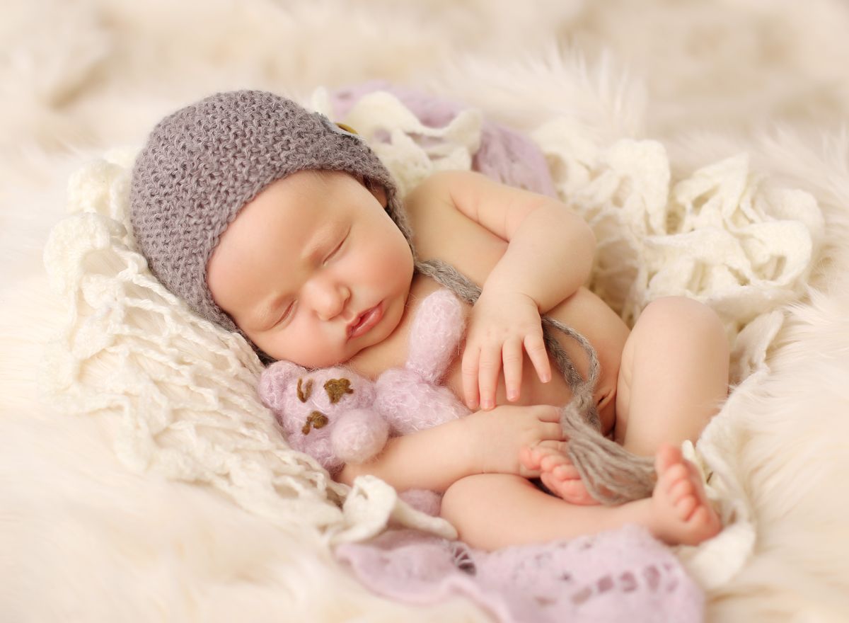 Spinkající novorozeně s háčkovaným medvídkem v náručí v ateliéru na newborn focení